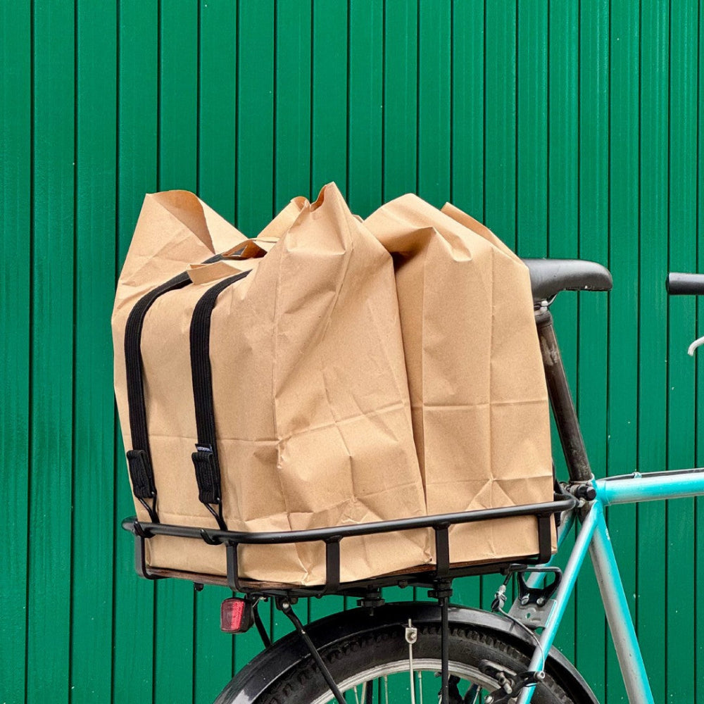 Ein Fahrrad mit dem Velokorb PACKI mit zwei Einkaufstaschen vor einem grünen Hintergrund